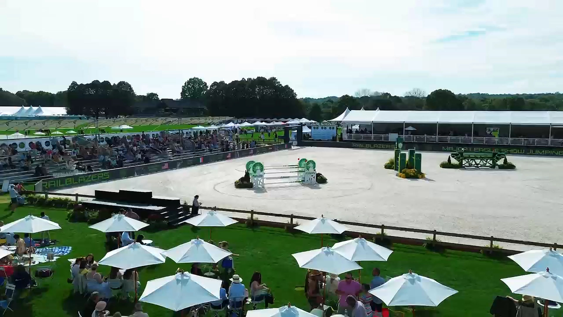 Aerial view of umbrella-shaded tables beside the show jumping ring
