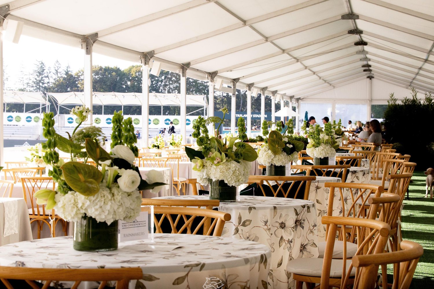 Round tables dressed with white flowers in the hospitality tent beside Trelawny Stadium