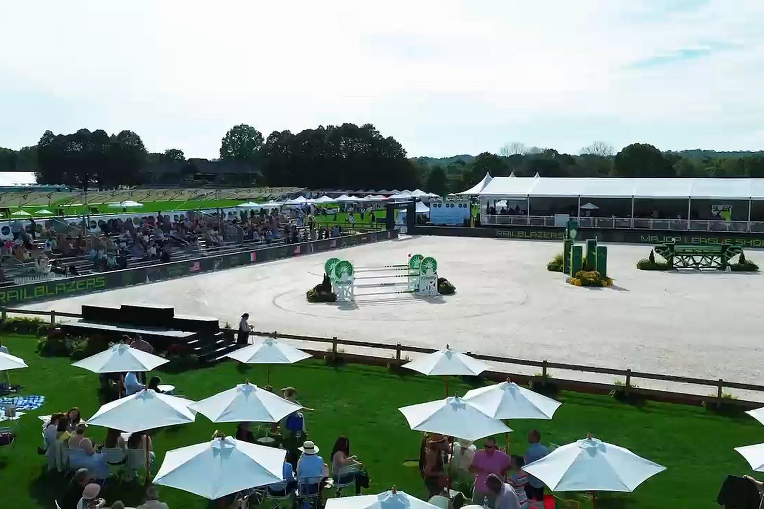 Aerial view of white umbrella tables on the lawn beside the show jumping ring